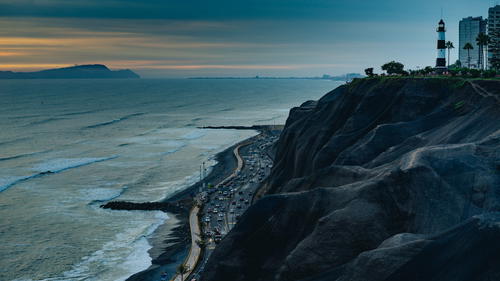 Gloomy sunset at black seaside cliffs with a black and white lighthouse and buildings