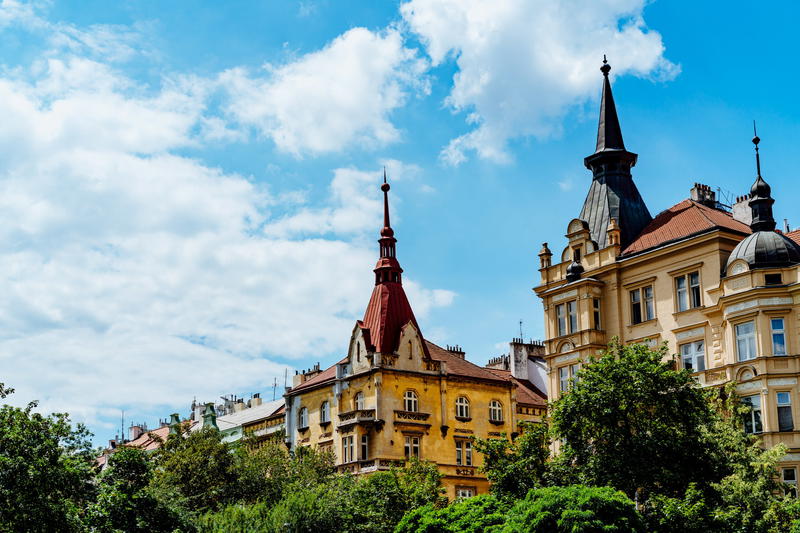 Green trees next to yellow and beige guildings with tall red and black spires