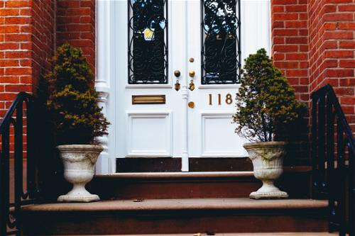 Small plants in white pots on the doorsteps of a brick brownstone row-home