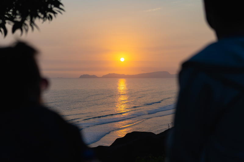 Silhouettes of two figures watching the sun set at the pacific ocean at the Malecon park of Lima, Peru