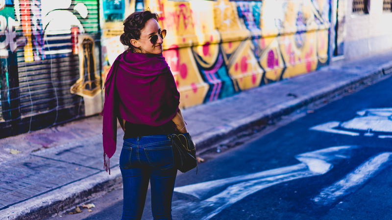 Woman wearing a magenta pashmina walking on a side street with murals in Buenos Aires