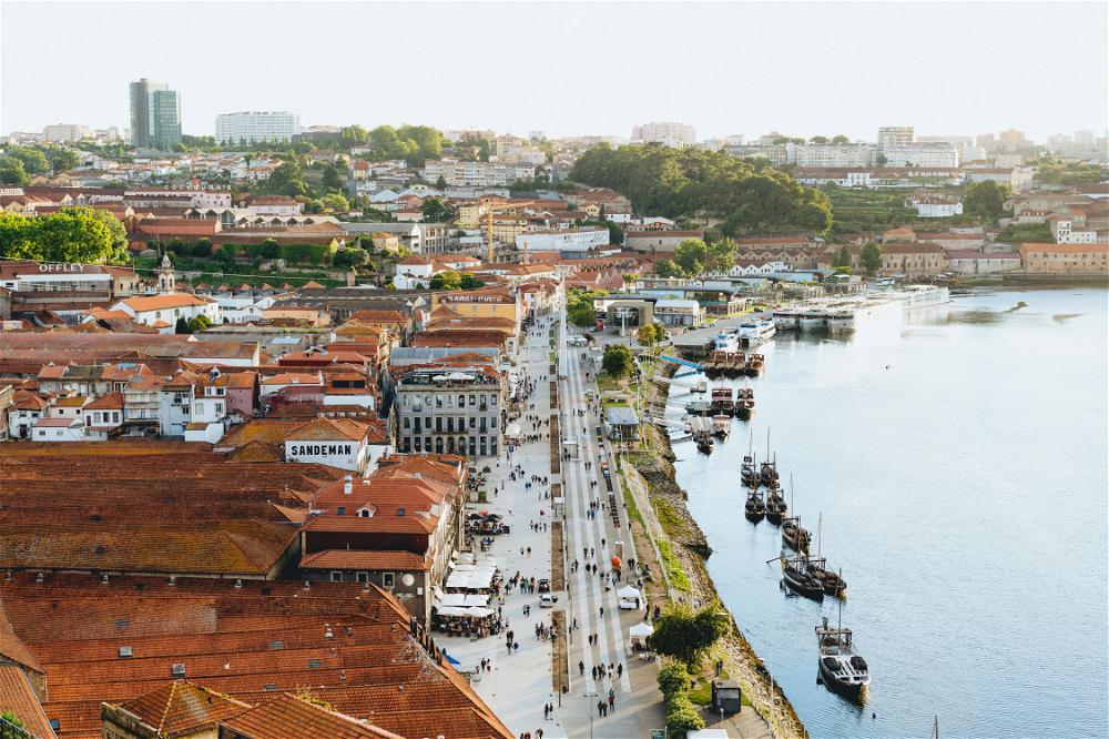 Red roofed white buildings and a pedestrian walkway full of people next to a river with boats