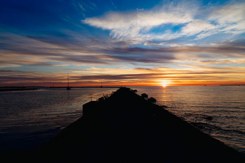 Shadow of a black rock jetty stretches into the Baltic Sea while the sun sets in Tallinn Estonia Pirita Beach