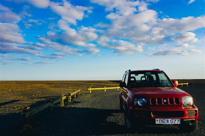 A red jeep parked on a gravel road.