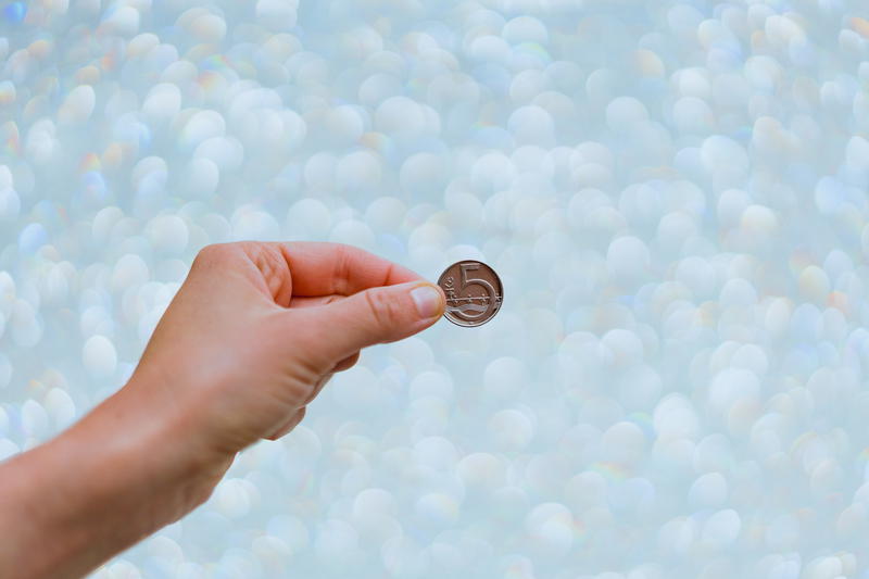 A person is holding a coin in front of a bokeh background.