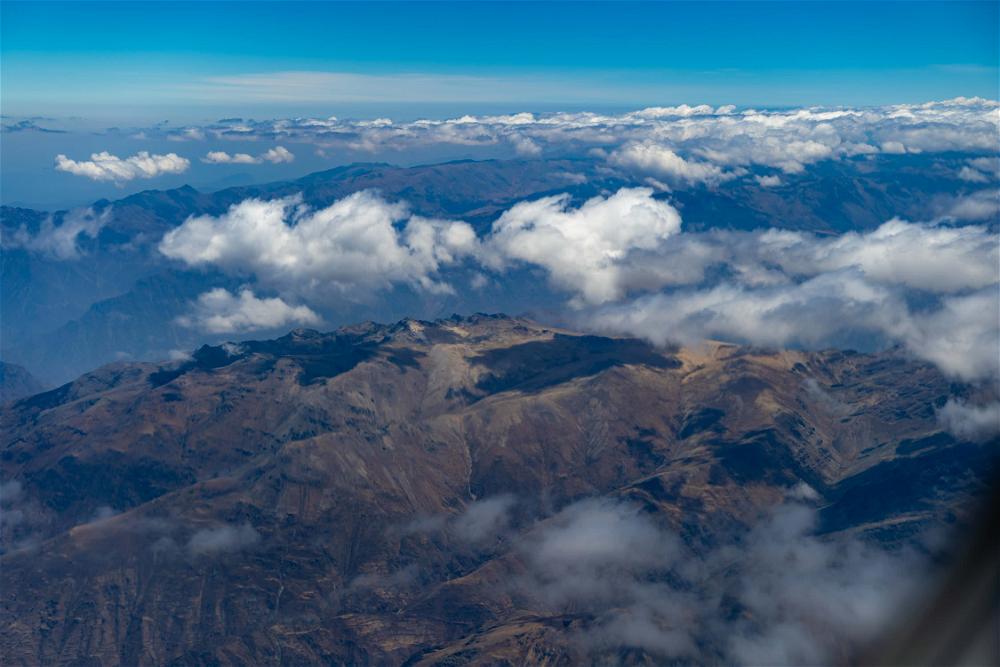 A view of mountains and clouds from an airplane wing.