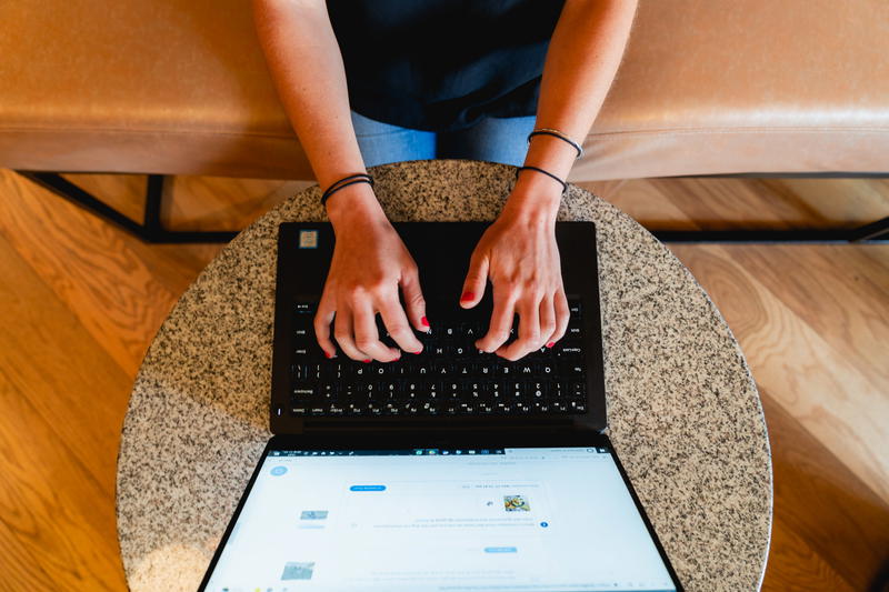 Woman sitting on a beige bench working remotely at a laptop at a small circular granite table