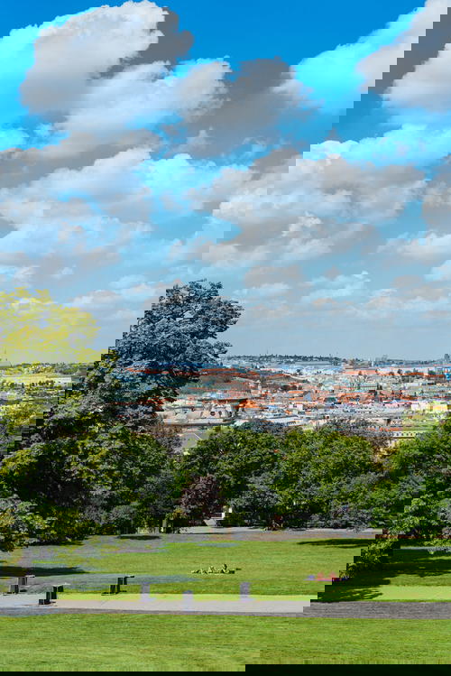 Green grassy areas of a park with buildings of Prague and a blue sky in the background