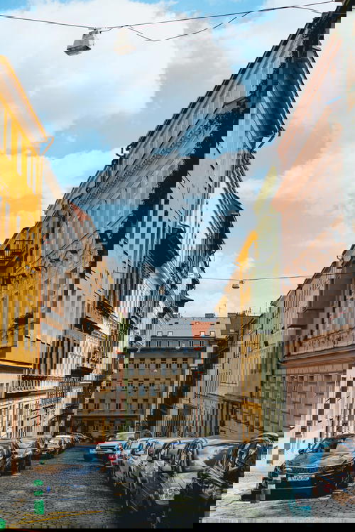 Pastel colored tall windowed buildings on a cobblestone street with a blue clear sky in Prague