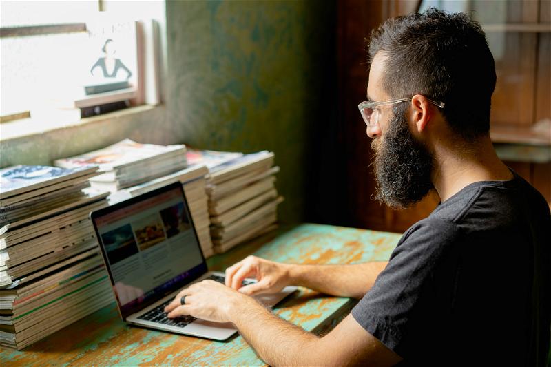 A man with a beard working on a laptop.