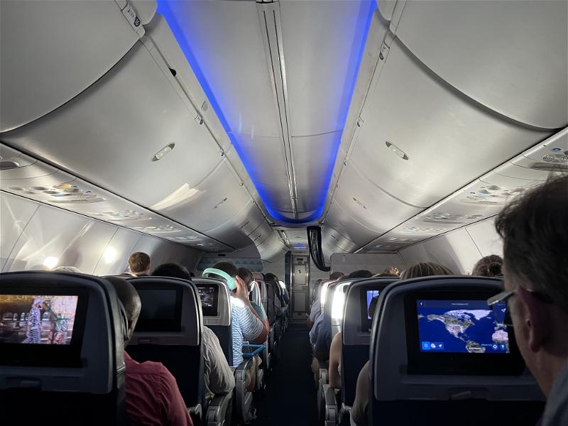 The inside of an airplane with people watching televisions.