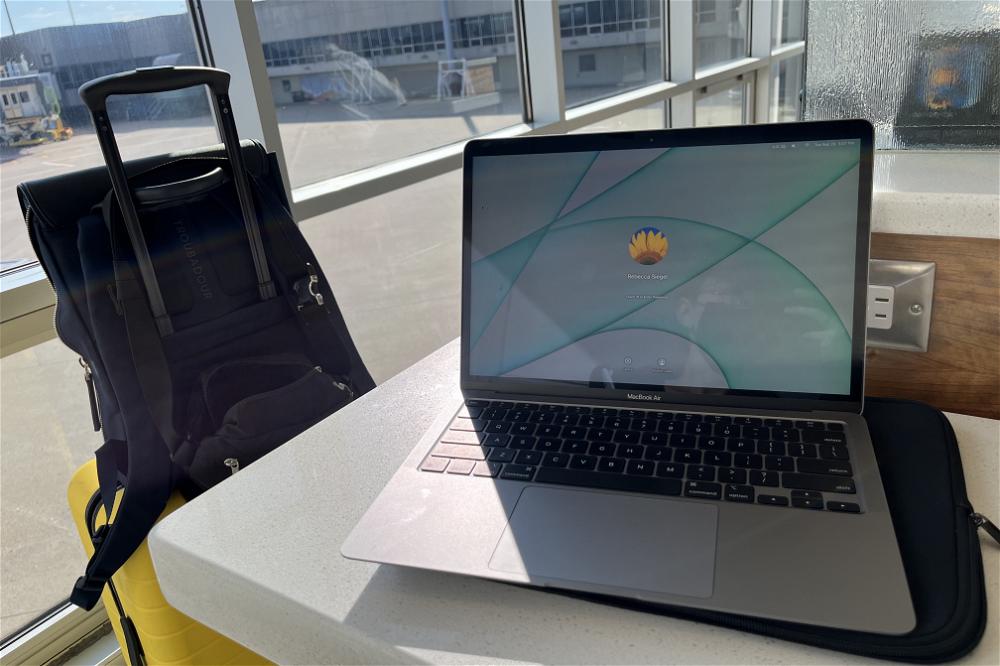 A laptop on a table next to a suitcase.
