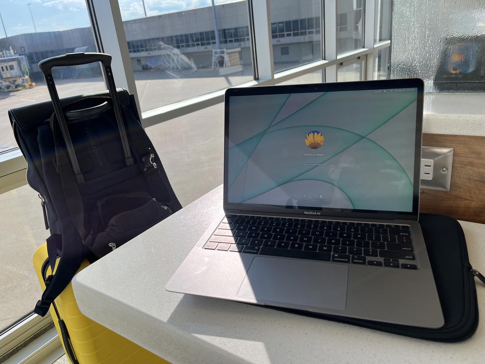 A laptop on a table next to a suitcase.