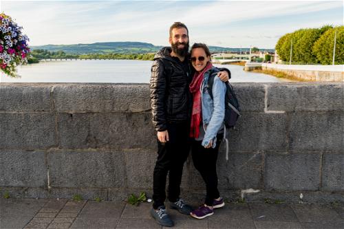 Bearded man and woman wearing sunglasses smiling on a stone bridge over a river in Limerick Ireland