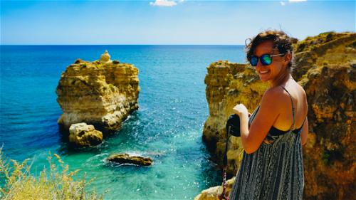A woman with turquoise and blue waters at a sandy beach with rock formations in Portugal