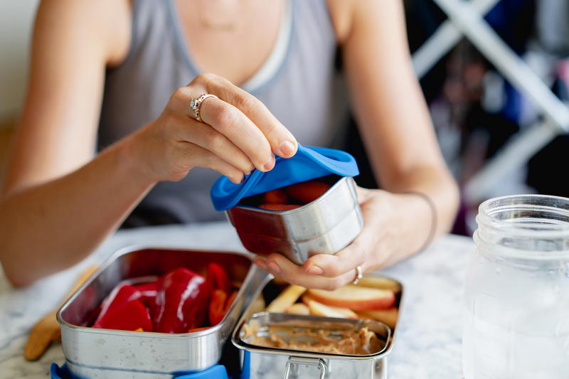 A woman is putting food into a lunch box.