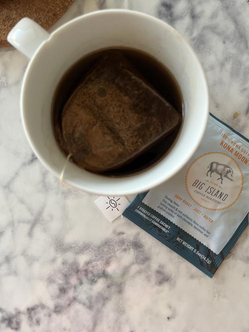 A cup of coffee sitting on a table next to a bag of tea.