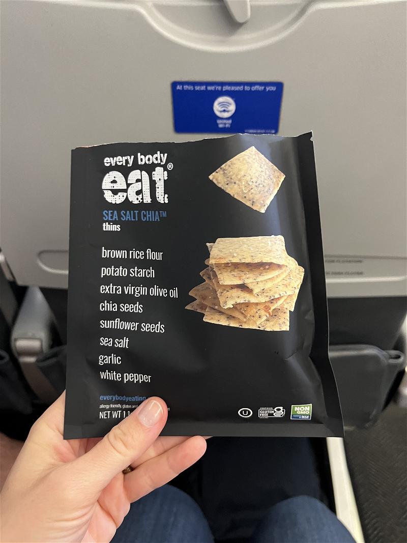 A person holding a bag of crackers on an airplane.