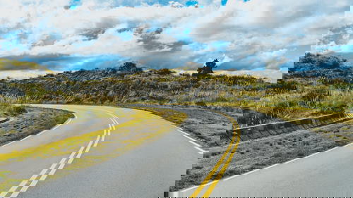 A road in the middle of a grassy field with a cloudy sky.