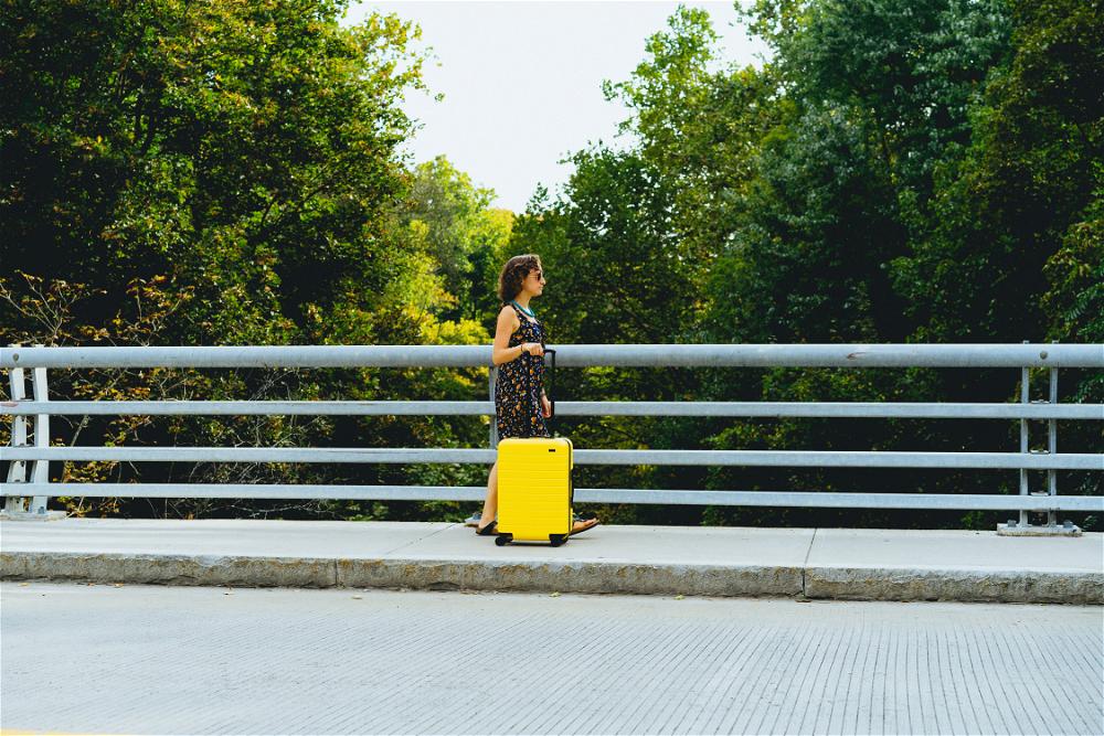 A woman standing on a bridge with a yellow suitcase.