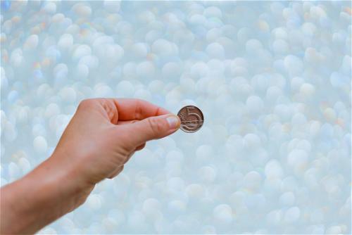 A person is holding a coin in front of a bokeh background.