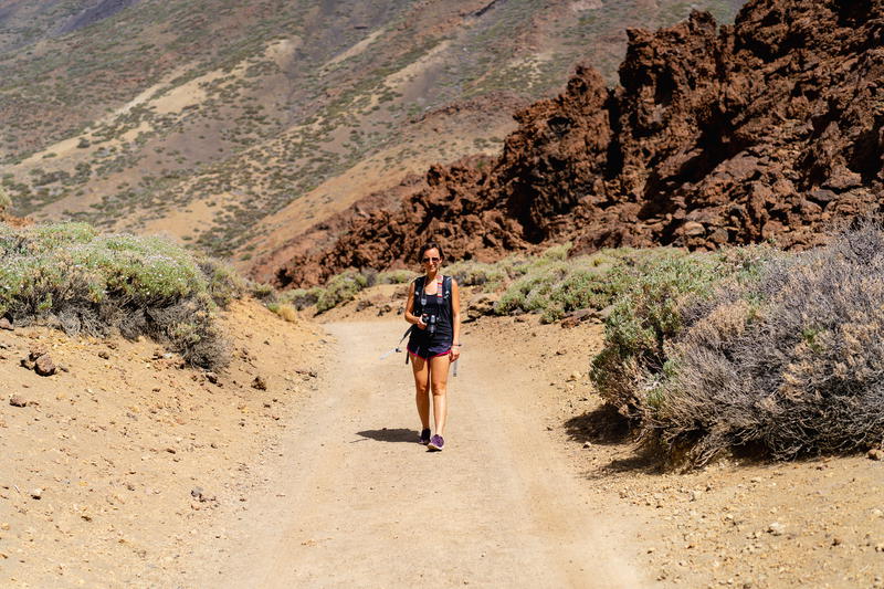 Woman hiking on a wide desert hiking trail with red desert rocks in El Teide National Park in Spain