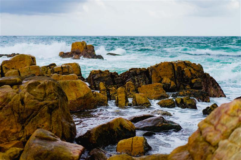 A rocky shore with waves and a cloudy sky.