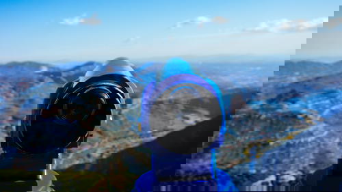 Blue binocular pointed toward a view of mountains and a blue sky with little white clouds