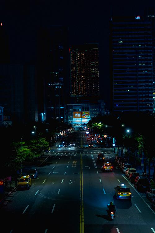 View of a main road with cars lined with trees and near skyscrapers at night