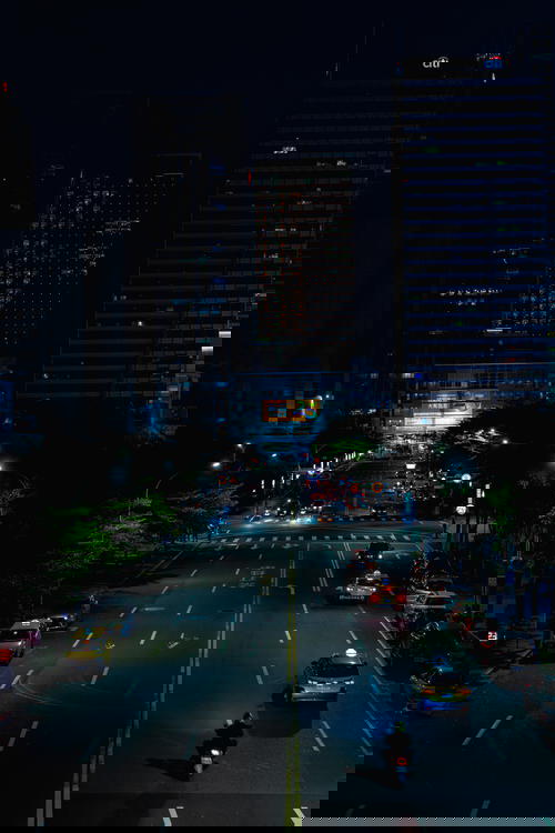 View of a main road with cars lined with trees and near skyscrapers at night