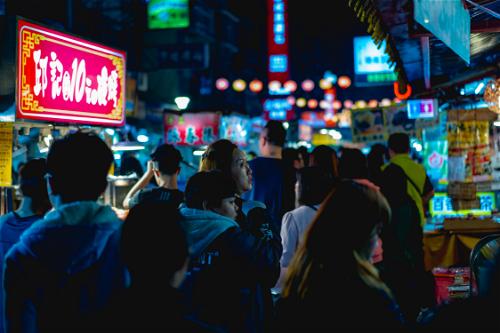 Neon signs of market vendors and crowds with neon lights at Raohe night market Taipei