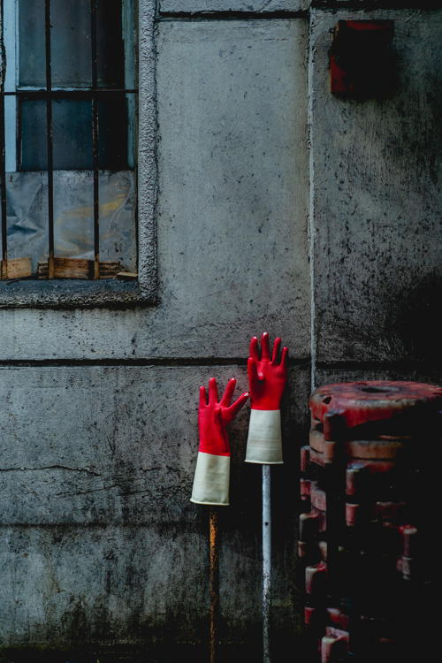 Red and white rubber gloves held up to dry on poles next to a wall