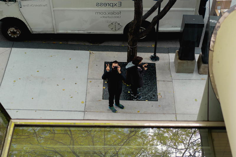 Two people standing on a sidewalk in Chicago next to a tree.