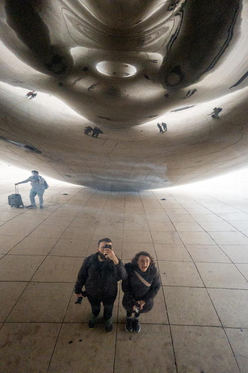 Two people standing in front of a large sculpture.