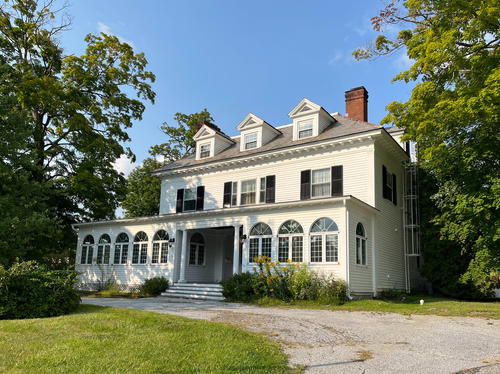 A white house with black shutters and a porch located in Lenox, Massachusetts.