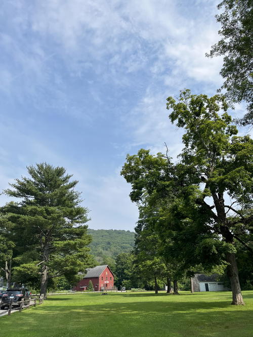 A grassy field with trees and a red barn in Litchfield, Connecticut.