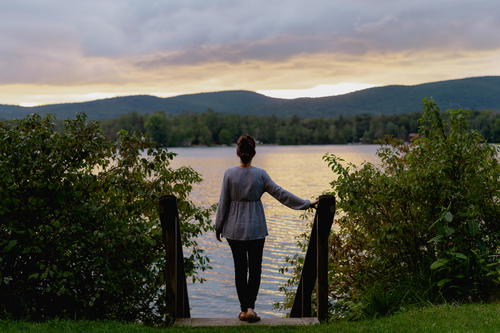 A woman standing on a wooden bridge in Pittsfield, Massachusetts, overlooking a lake at sunset.