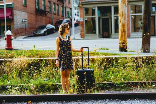 A woman standing next to a train track in Beacon with a suitcase.