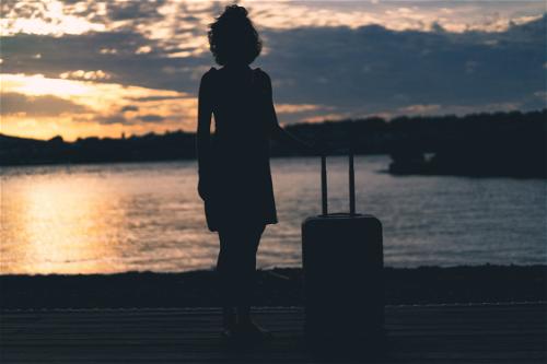 A woman holding a suitcase silhouetted against the sunset in Beacon, New York.