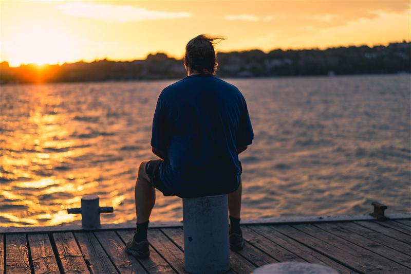 A man sitting on a dock in New York at sunset.