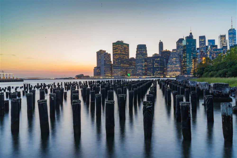Manhattan skyline at sunset with wooden posts in the water, featuring NYC.