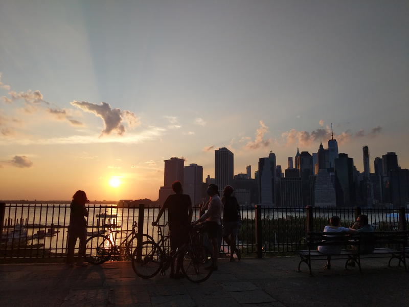A group of people are sitting on a bench in front of the Brooklyn skyline.