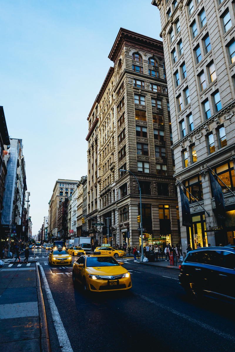 A yellow cab driving down a NYC city street.