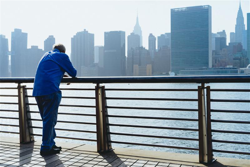 A man is standing on a railing admiring NYC's skyline.