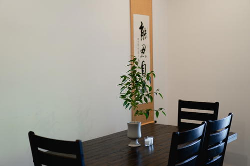 Three black chairs placed at a dining table with a plant in the center and a Chinese calligraphy painting on the wall