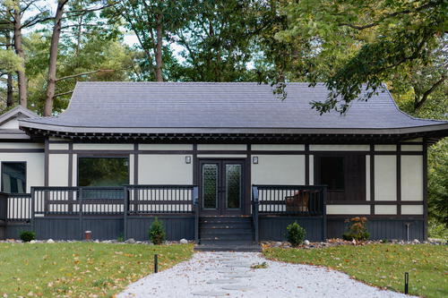 A Japanese-style simple pagoda house with large square windows and two doors at the center, and a black wooden deck