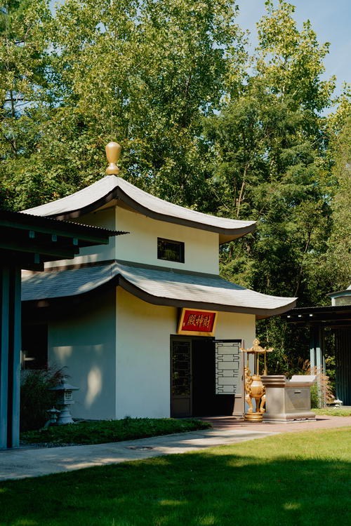 Green trees behind a simple Chinese-style white pagoda with brown roofing and a gold dome on top