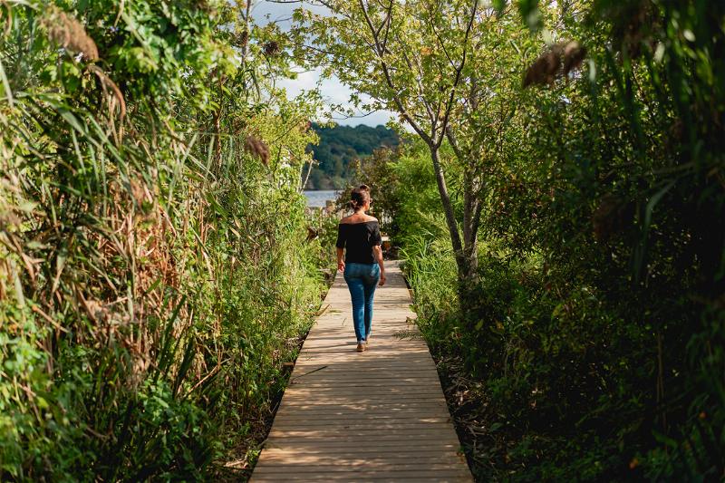 A woman wearing a black shirt and jeans walking the boardwalk path to Saugerties Lighthouse on the Hudson River
