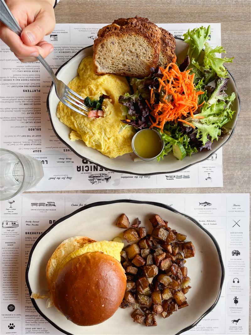 A hand and a fork with a breakfast omelet and salad, and an egg sandwich with hash brows at the Phoenicia Diner