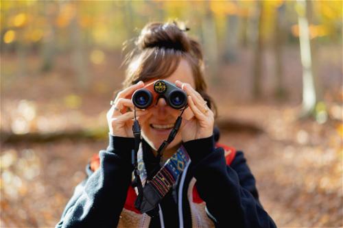 A woman using binoculars in the woods near New York City.